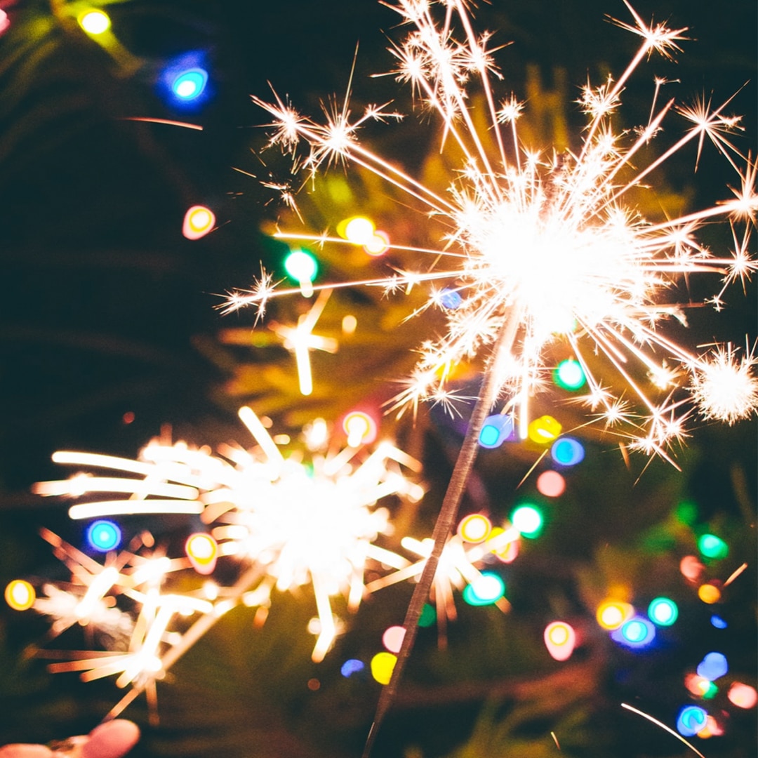 Sparkler against a dark background with colourful lights.